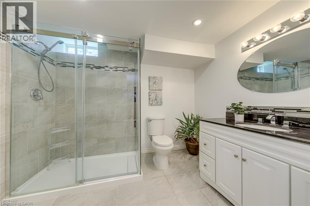 Full bathroom with a glass-enclosed shower featuring light-toned tilework and a decorative accent band - 2380 Woodcrest Drive, Oakville, ON - Indoor Photo Showing Bathroom