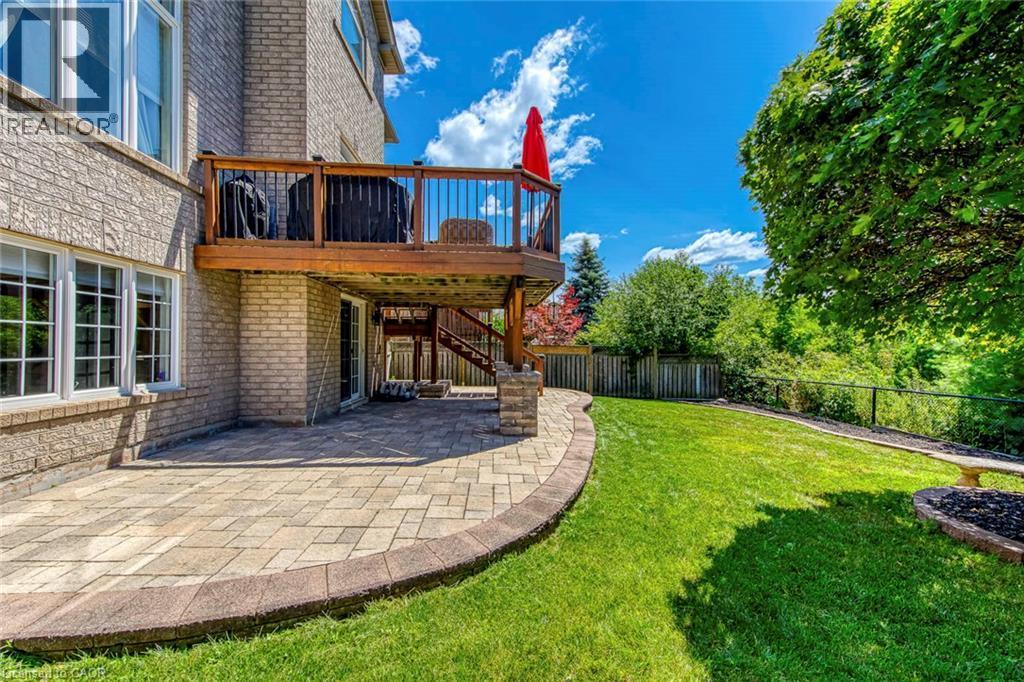 Expansive backyard featuring a manicured lawn, a raised wooden deck with dark railings, a ground-level patio with stone pavers, and mature trees providing natural screening - 2380 Woodcrest Drive, Oakville, ON - Outdoor
