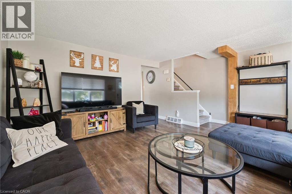 Spacious living area featuring wood-finish flooring, light neutral wall paint, and a built-in staircase with carpeted treads - 589 Elgin Street N, Cambridge, ON - Indoor Photo Showing Living Room