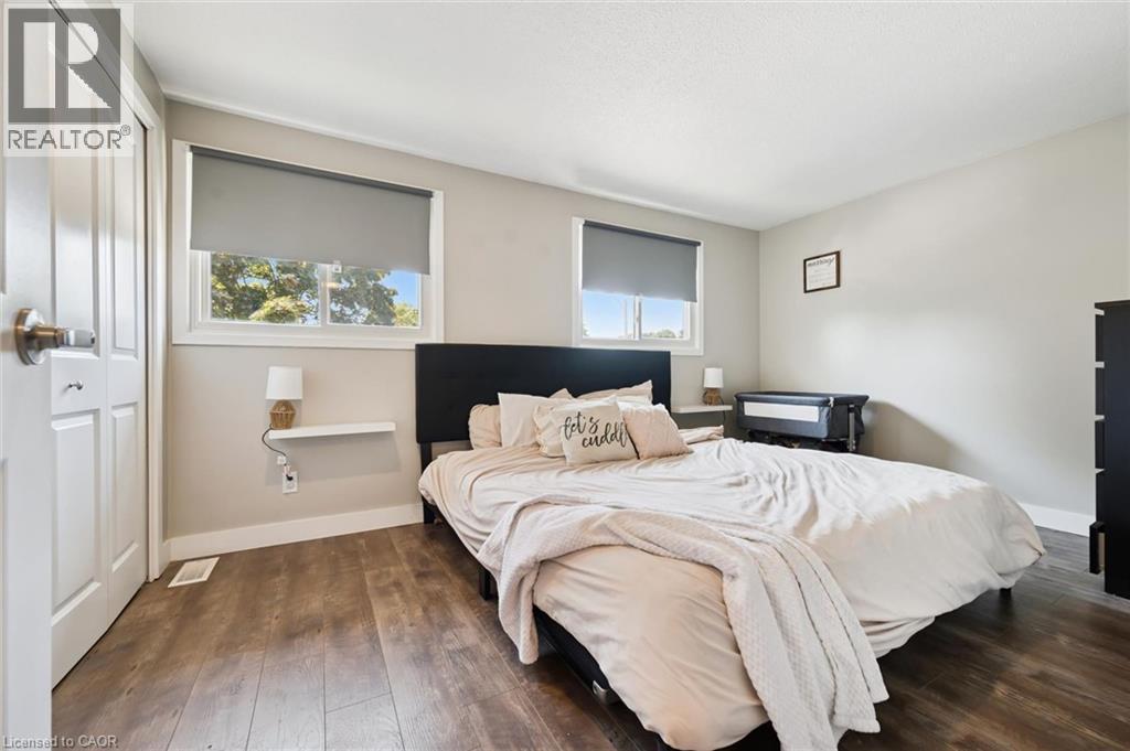 Bedroom featuring wood-finish flooring, two large windows with roller shades, and light-toned walls - 589 Elgin Street N, Cambridge, ON - Indoor Photo Showing Bedroom