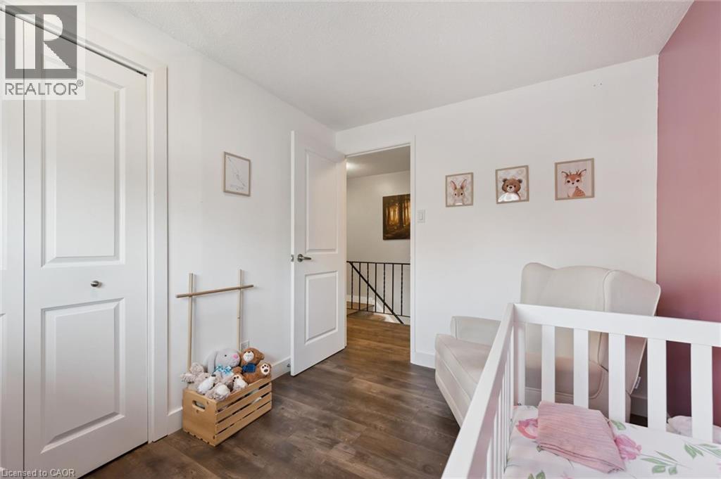 Interior room featuring wood-finish flooring and white walls with an accent wall in a soft pink hue - 589 Elgin Street N, Cambridge, ON - Indoor Photo Showing Bedroom