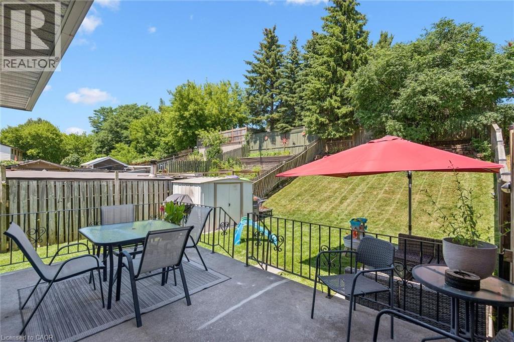 Concrete patio space featuring a wrought iron railing, a tiered backyard with a manicured lawn, and mature perimeter trees - 589 Elgin Street N, Cambridge, ON - Outdoor