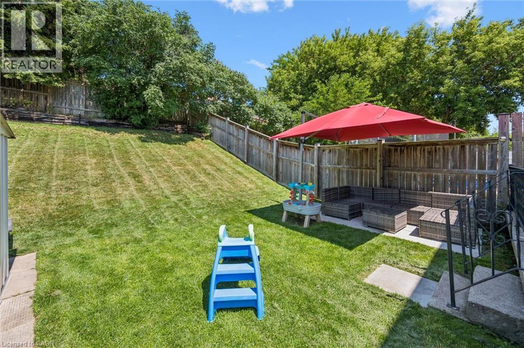 Expansive backyard featuring a large grassy area, privacy fencing, mature trees, and a paved patio area - 589 Elgin Street N, Cambridge, ON - Outdoor With Backyard