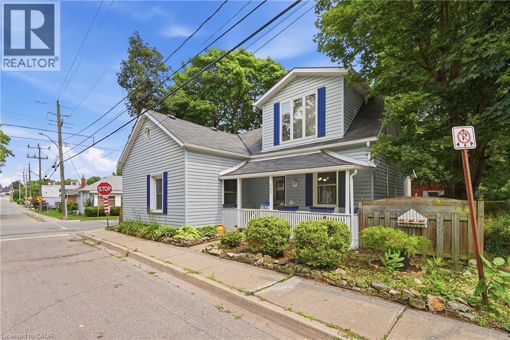 Light blue siding exterior featuring a covered front porch with white railing, blue window shutters, and mature trees - 153 Montrose Street N, Cambridge, ON - Outdoor