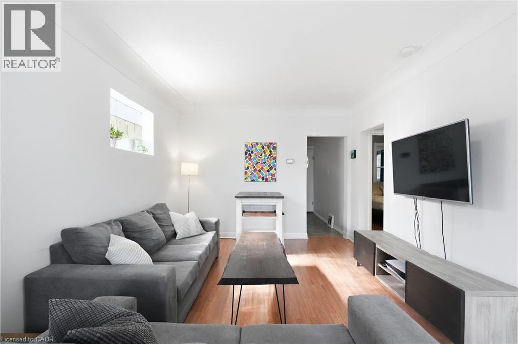 Bright living space featuring warm wood-finish flooring, white painted walls, and a window providing natural light - 58 Edinburgh Avenue, Hamilton, ON - Indoor Photo Showing Living Room