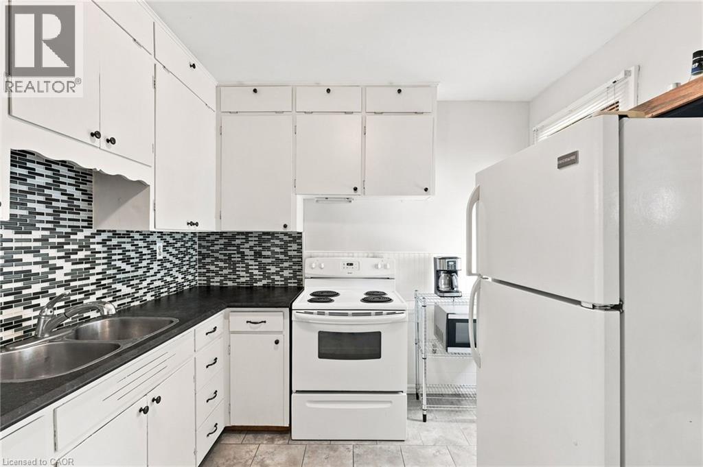 Kitchen featuring white cabinetry with dark hardware, dark countertops, and a mosaic tile backsplash - 58 Edinburgh Avenue, Hamilton, ON - Indoor Photo Showing Kitchen With Double Sink