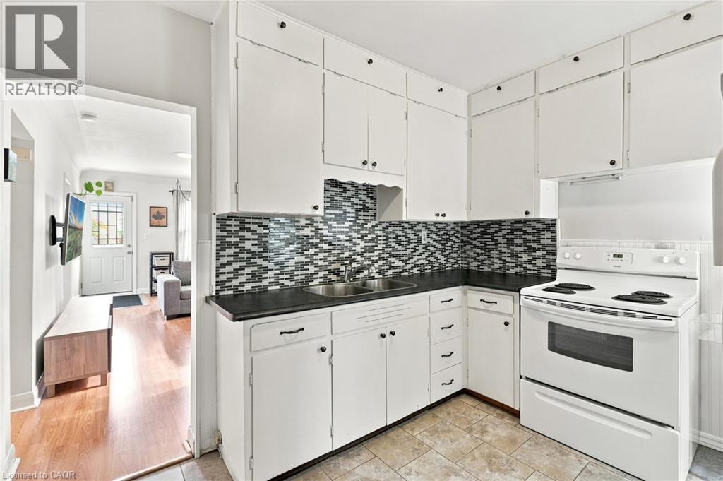 Kitchen featuring white cabinetry, dark countertops, a mosaic tile backsplash, a white electric range, and tile flooring - 58 Edinburgh Avenue, Hamilton, ON - Indoor Photo Showing Kitchen With Double Sink
