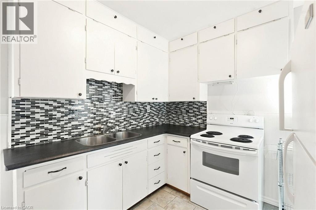 Kitchen featuring white cabinetry, black countertops, a mosaic tile backsplash, double basin stainless steel sink, and a white electric range - 58 Edinburgh Avenue, Hamilton, ON - Indoor Photo Showing Kitchen With Double Sink