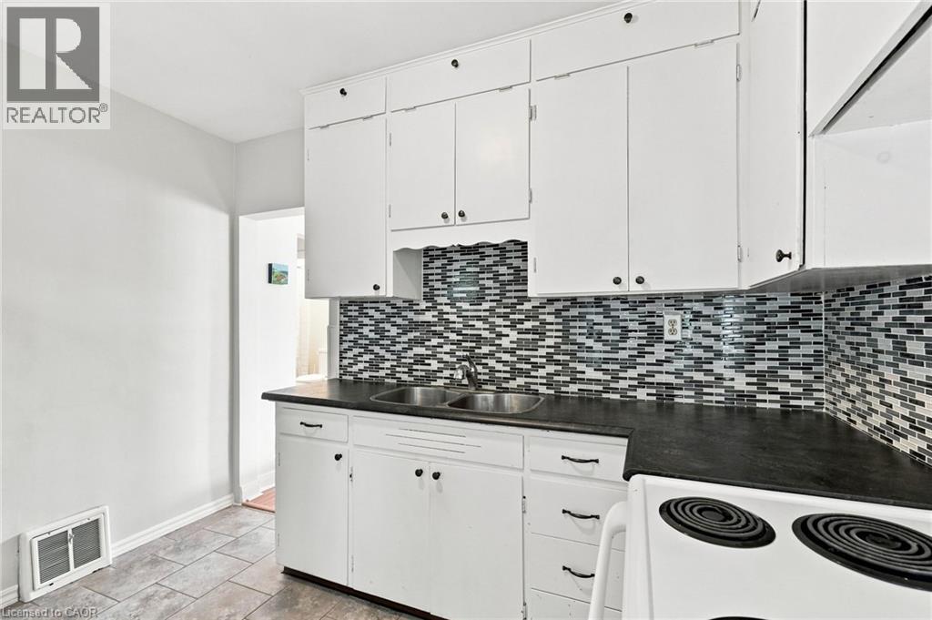 Kitchen featuring white cabinetry, a dual basin stainless steel sink, dark countertops, and a mosaic tile backsplash - 58 Edinburgh Avenue, Hamilton, ON - Indoor Photo Showing Kitchen With Double Sink