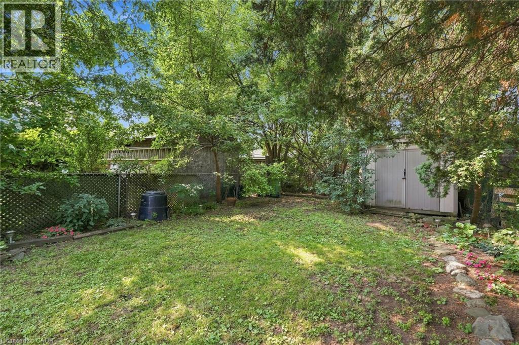 Expansive grassy yard area with perimeter fencing, mature trees, a storage shed, and stone garden bed edging - 58 Edinburgh Avenue, Hamilton, ON - Outdoor