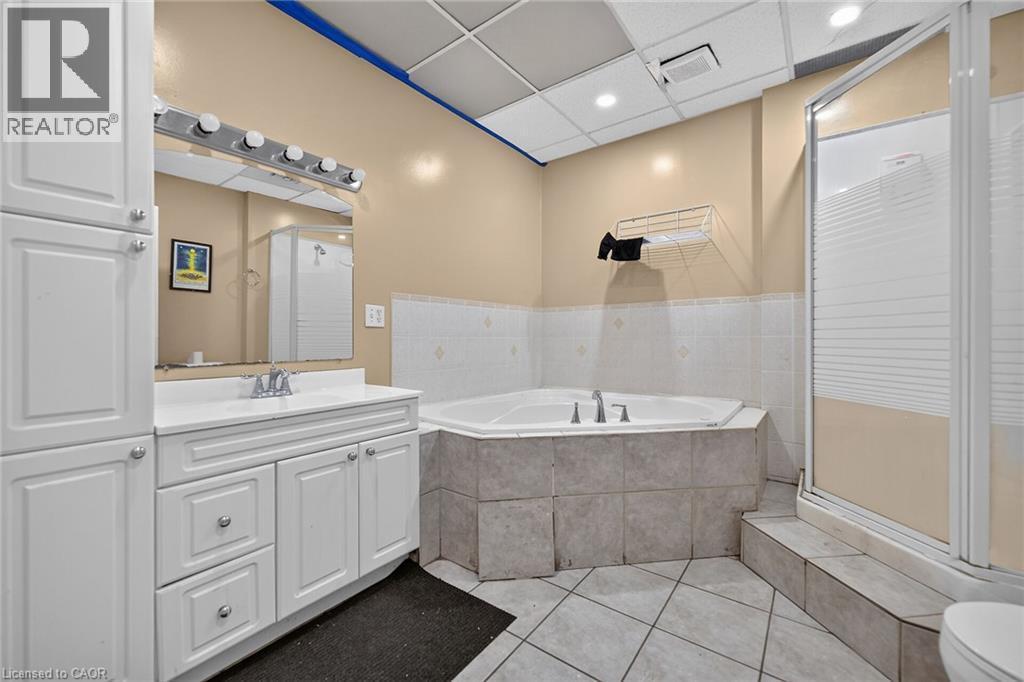 Bathroom featuring a white vanity with integrated sink, a built-in jetted tub, a separate shower enclosure, tiled flooring, and a drop ceiling with recessed lighting - 1292 Barton Street E, Hamilton, ON