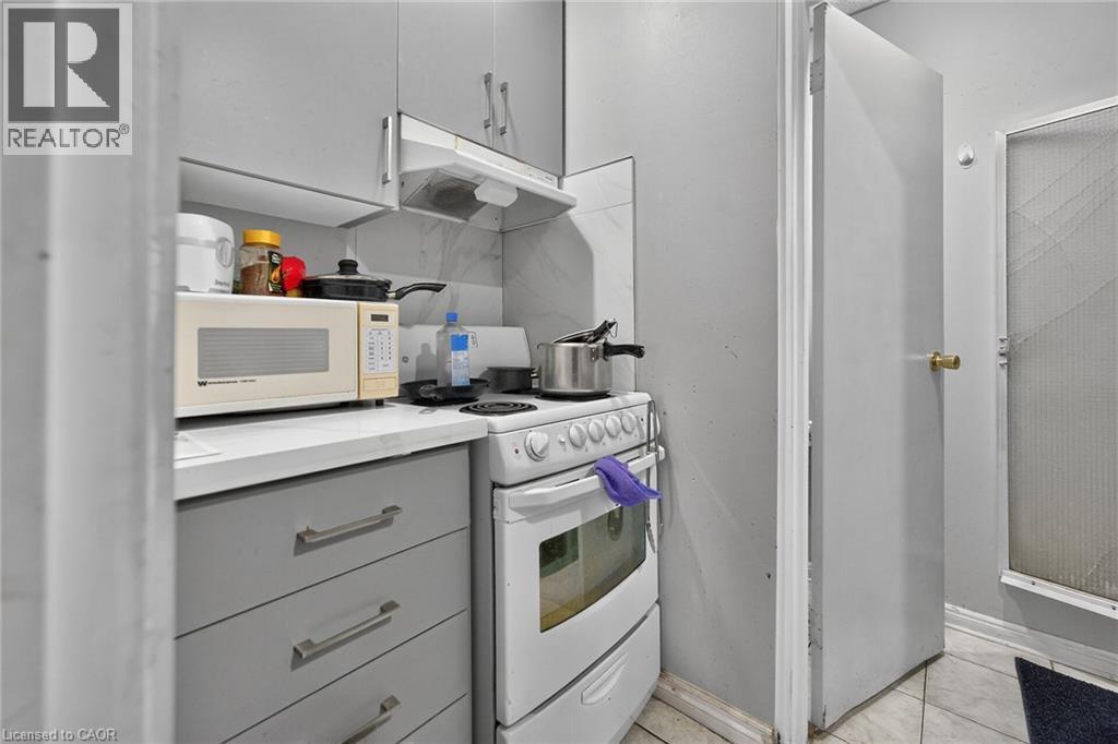 Compact kitchen space featuring light gray cabinetry, white countertops, and a white electric range with an overhead exhaust fan - 1292 Barton Street E, Hamilton, ON