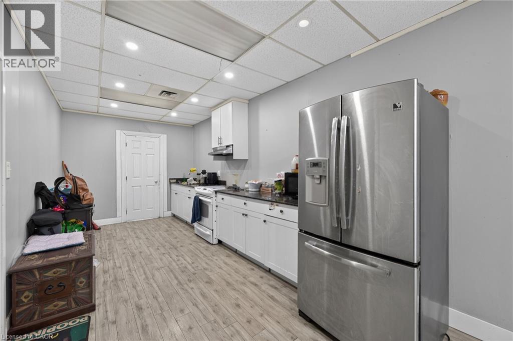 Kitchen featuring wood-finish flooring, white cabinetry, dark countertops, and a stainless steel French door refrigerator - 1292 Barton Street E, Hamilton, ON