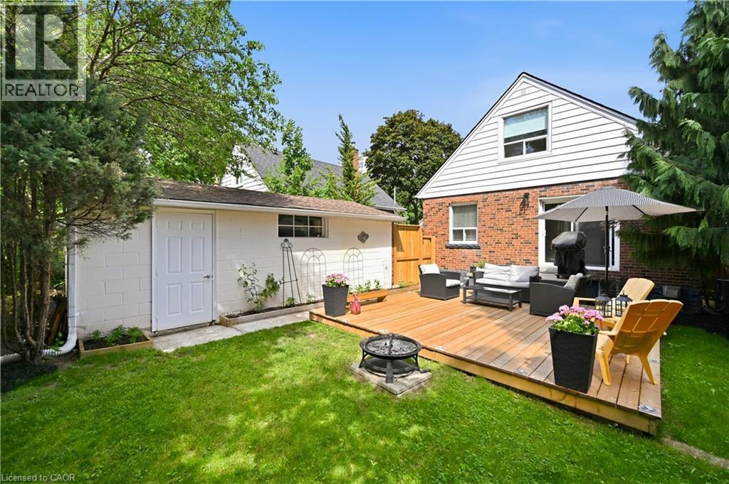 Expansive backyard featuring a large wooden deck, a built-in fire pit, manicured lawn, and mature perimeter trees - 18 Ipswich Place, Hamilton, ON - Outdoor With Deck Patio Veranda With Exterior