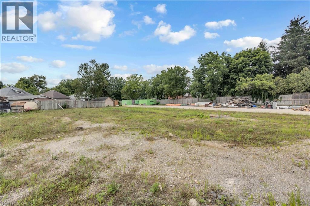 Vacant land parcel featuring a mix of gravel and natural growth, bordered by mature trees and fencing - 9 James Street, Simcoe, ON