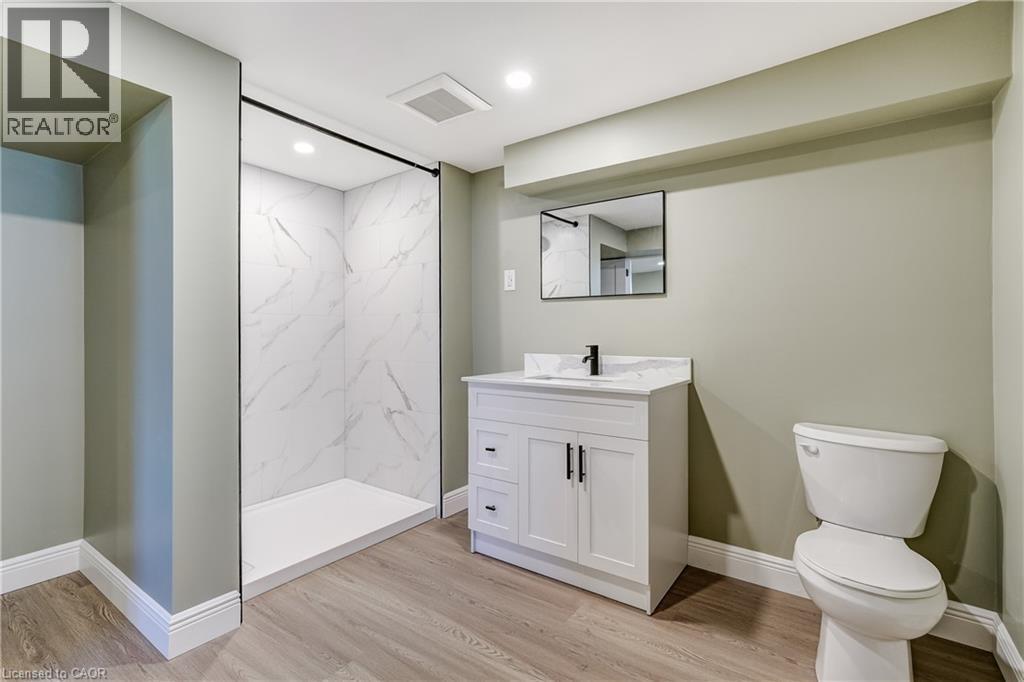 Bathroom featuring a walk-in shower with white marbled wall panels, a white vanity with a rectangular sink, a black-framed mirror, and light wood-finish flooring - 191 Glenmor Drive, Caledonia, ON - Indoor Photo Showing Bathroom
