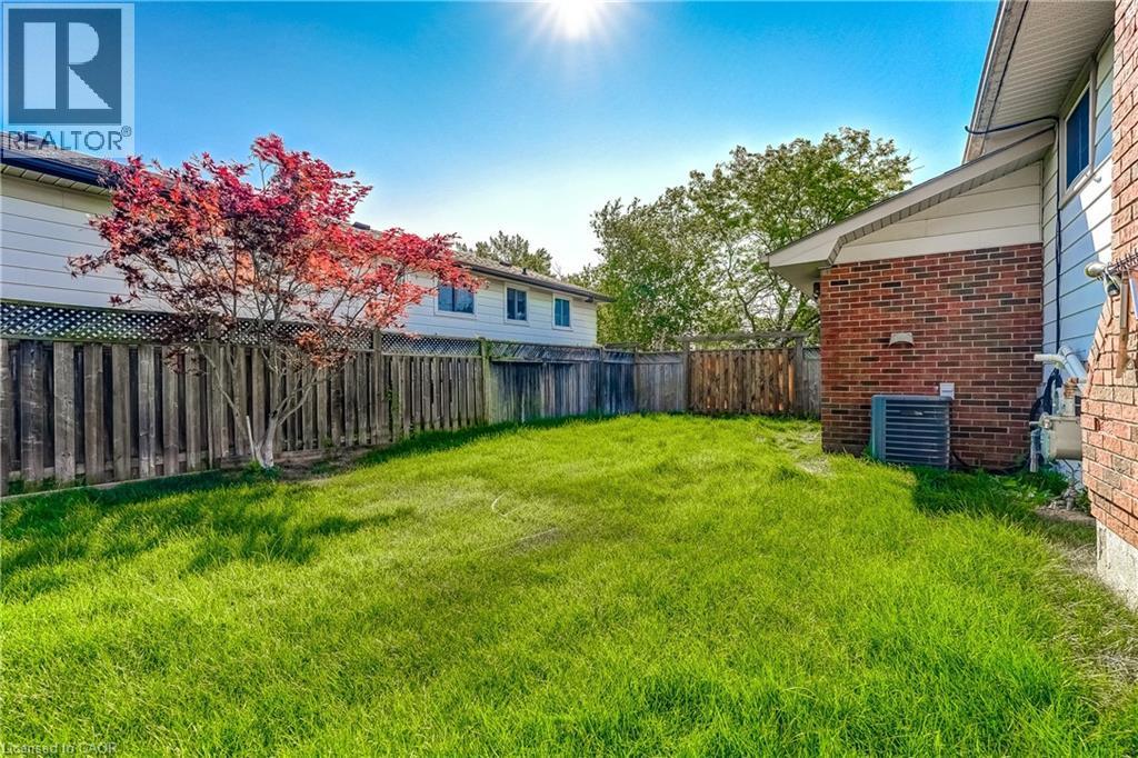 Expansive backyard featuring a green lawn, wood privacy fencing, and a mature tree with vibrant red foliage - 191 Glenmor Drive, Caledonia, ON - Outdoor