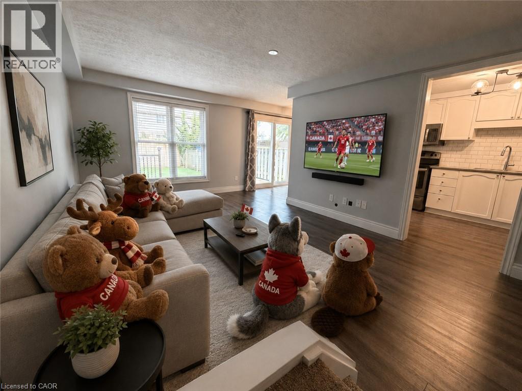 Open-concept living space featuring wood-finish flooring, a contemporary kitchen with white cabinetry and subway tile backsplash, a sliding glass door to a patio, and a large window with blinds - 41 Edgemere Drive, Cambridge, ON - Indoor Photo Showing Living Room