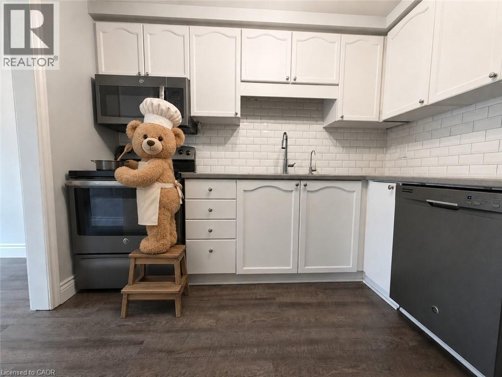 Modern kitchen featuring white cabinetry, subway tile backsplash, dark countertops, and wood-finish flooring - 41 Edgemere Drive, Cambridge, ON - Indoor Photo Showing Kitchen