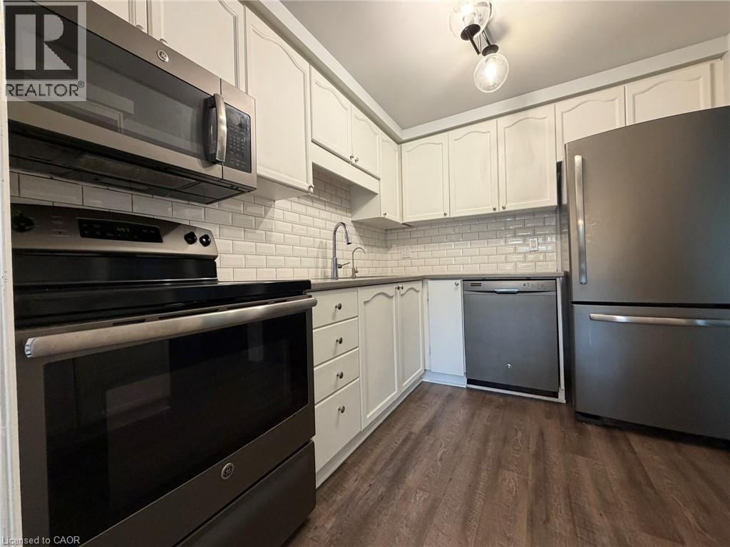 Kitchen featuring stainless steel appliances, white subway tile backsplash, white cabinetry, dark countertops, and wood-finish flooring - 41 Edgemere Drive, Cambridge, ON - Indoor Photo Showing Kitchen