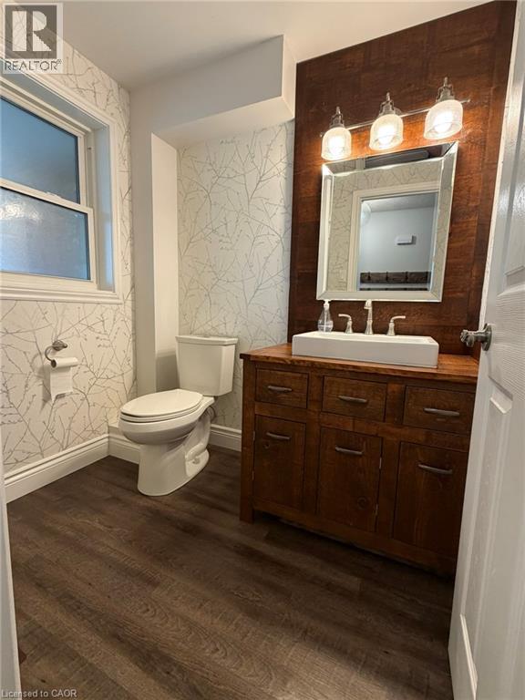Bathroom featuring a rectangular vessel sink, wood-finish vanity, wood-finish flooring, patterned wallpaper, and a window for natural light - 41 Edgemere Drive, Cambridge, ON - Indoor Photo Showing Bathroom