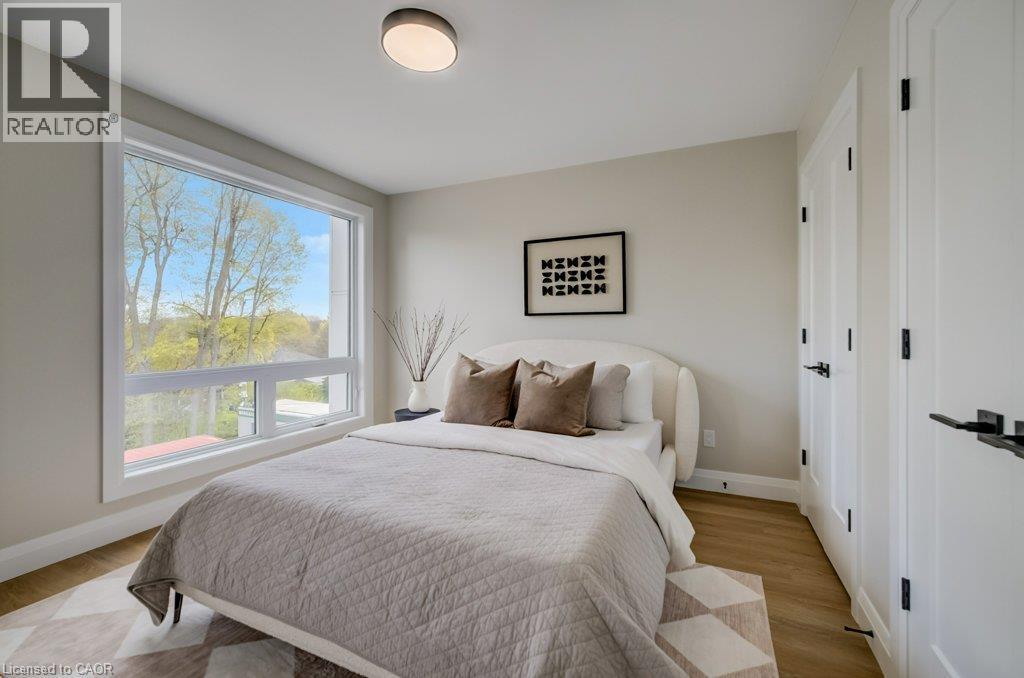 Bright room featuring a large rectangular window, wood-finish flooring, two white panel doors with black hardware, and a ceiling-mounted light fixture - 210 Heritage Drive Unit# Upper, Kitchener, ON - Indoor Photo Showing Bedroom