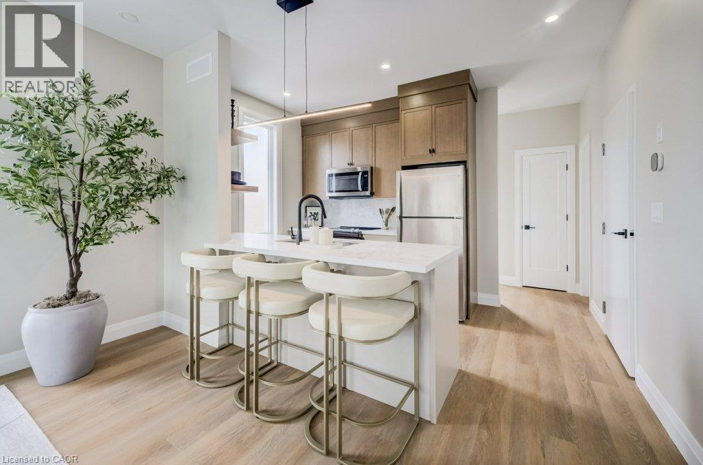 Modern kitchen featuring light wood-finish cabinetry, stainless steel appliances, a white countertop island with seating, and wood-finish flooring - 210 Heritage Drive Unit# Upper, Kitchener, ON - Indoor Photo Showing Kitchen