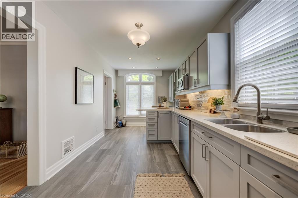 Galley kitchen featuring light gray cabinetry, stainless steel appliances, a double basin sink, light-toned countertops, and wood-finish flooring - 314 Glasgow Street, Kitchener, ON - Indoor Photo Showing Kitchen With Double Sink