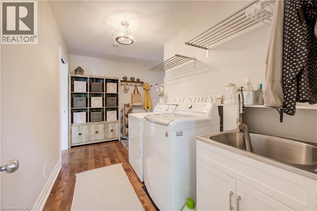 Dedicated laundry area featuring wood-finish flooring, a stainless steel utility sink with a pull-down faucet, and built-in shelving - 314 Glasgow Street, Kitchener, ON - Indoor Photo Showing Laundry Room