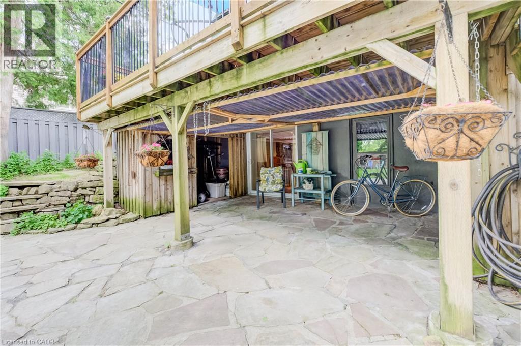 Stone patio featuring a covered seating area beneath a wood-frame deck with dark metal railings - 314 Glasgow Street, Kitchener, ON -