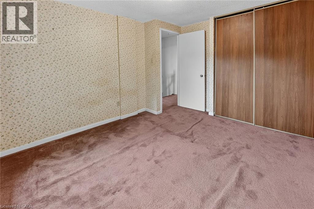 Carpeted room featuring a white door, sliding wood-finish closet doors, patterned wallpaper, and white baseboards - 125 Bonaventure Drive Unit# 50, Hamilton, ON - Indoor Photo Showing Other Room