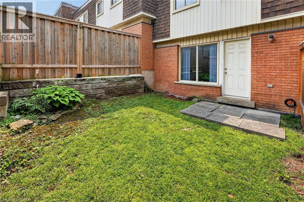 Private backyard space featuring a wood fence, a retaining wall with integrated plantings, and a grass lawn - 125 Bonaventure Drive Unit# 50, Hamilton, ON - Outdoor With Exterior