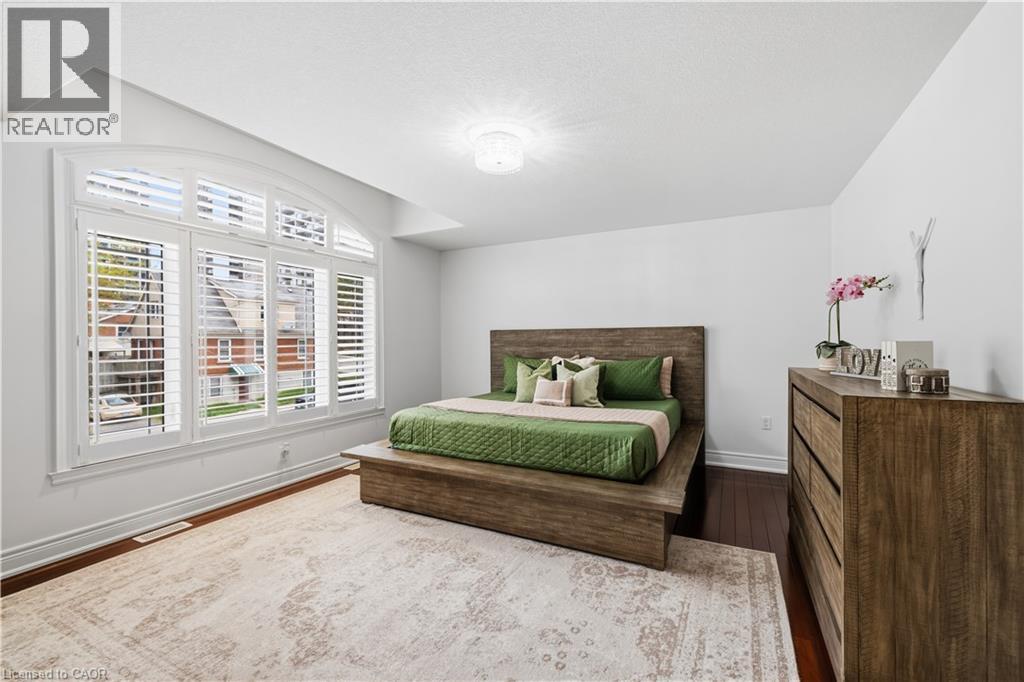 Spacious room featuring an arched window with integrated white plantation shutters, dark wood-finish flooring, a contemporary ceiling light fixture, and white painted walls - 199 Hunter Street W, Hamilton, ON - Indoor Photo Showing Bedroom