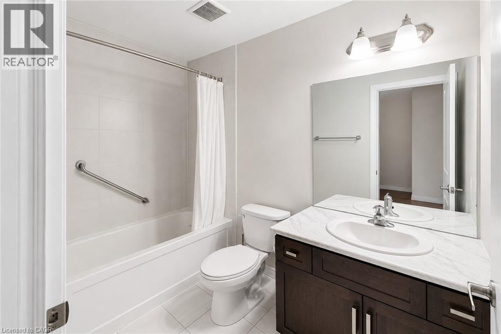 Full bathroom featuring a white porcelain tub with tiled surround, a toilet, and a vanity with a white countertop and dark wood-finish cabinetry - 133 St Leger Street, Kitchener, ON - Indoor Photo Showing Bathroom