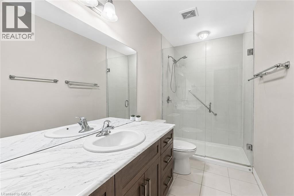 Bathroom featuring a dual-sink vanity with a white-veined countertop, dark wood-finish cabinetry, and an expansive wall-mounted mirror - 133 St Leger Street, Kitchener, ON - Indoor Photo Showing Bathroom