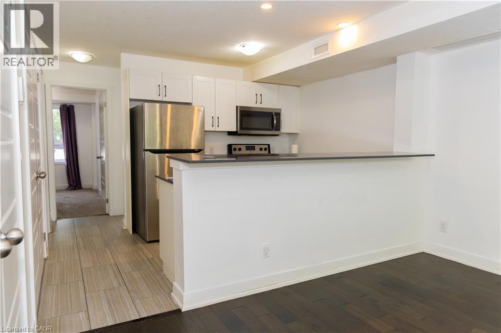 Kitchenette featuring white cabinetry, stainless steel appliances, dark countertops, and a breakfast bar - 190 Century Hill Drive Unit# A5, Kitchener, ON - Indoor Photo Showing Kitchen