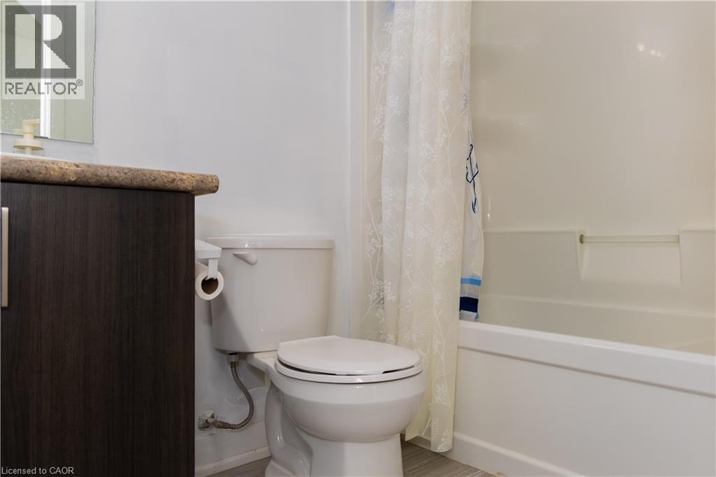 Bathroom featuring a dark wood-finish vanity with a speckled countertop, a white toilet, and a white tub with integrated shelving - 190 Century Hill Drive Unit# A5, Kitchener, ON - Indoor Photo Showing Bathroom