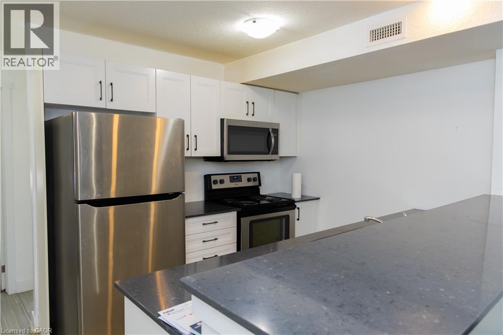 Kitchen featuring stainless steel appliances, white cabinetry with dark hardware, a dark countertop, a built-in microwave, and an integrated range with an oven - 190 Century Hill Drive Unit# A5, Kitchener, ON - Indoor Photo Showing Kitchen