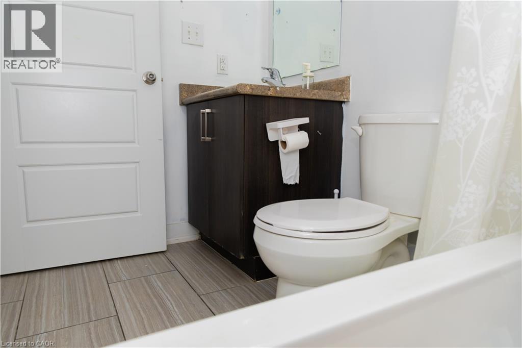 Bathroom featuring wood-finish tile flooring, a white paneled door, a dark wood-finish vanity with a light-colored countertop, and a white toilet - 190 Century Hill Drive Unit# A5, Kitchener, ON - Indoor Photo Showing Bathroom