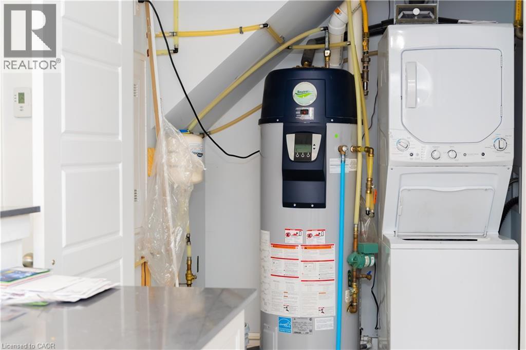 Dedicated utility area featuring a stacked washer and dryer, a water heater, and visible plumbing - 190 Century Hill Drive Unit# A5, Kitchener, ON - Indoor Photo Showing Laundry Room
