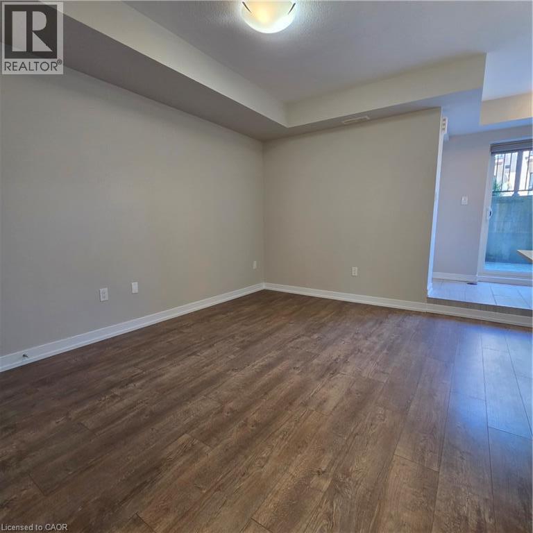 Expansive room featuring wood-finish flooring, light neutral wall paint, white baseboards, and a semi-flush mount ceiling light - 20 Palace Place Unit# E9, Kitchener, ON - Indoor Photo Showing Other Room