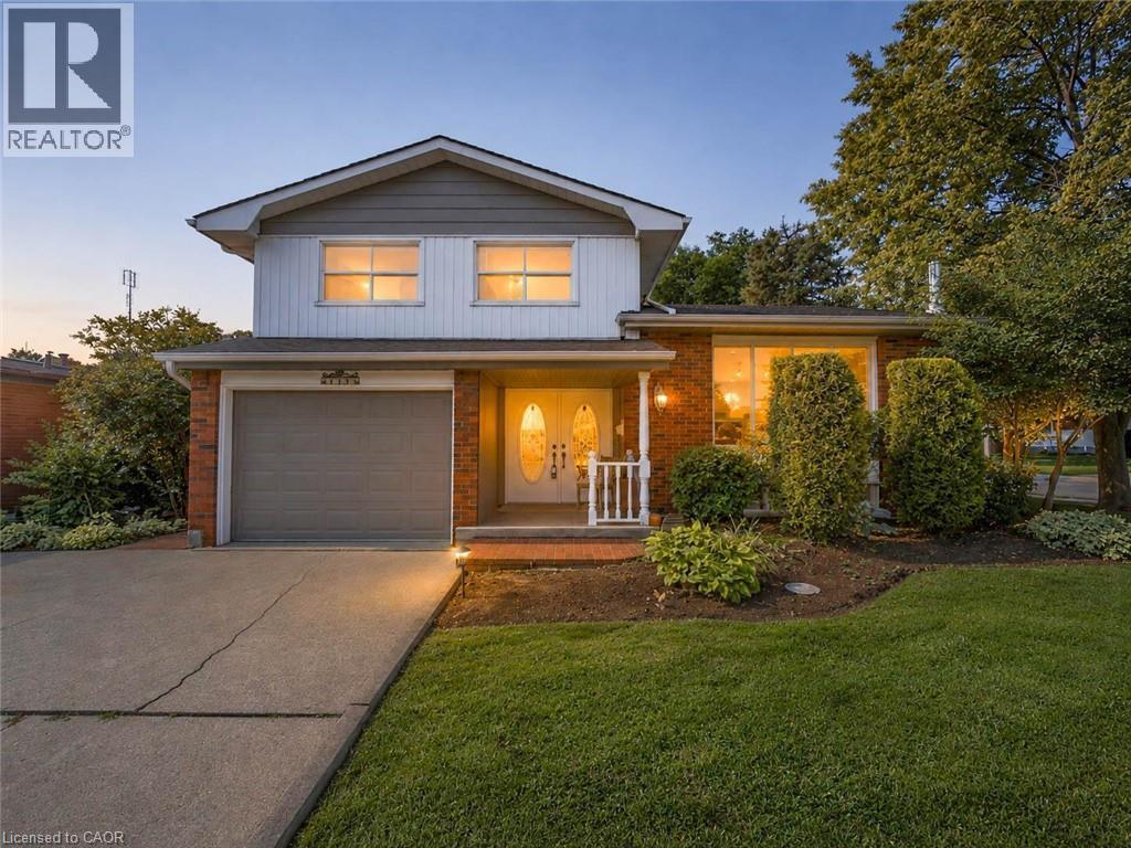 Two-story residence featuring a brick and siding exterior, an attached garage with a roll-up door, a concrete driveway, a manicured lawn, and mature landscaping - 143 Cromwell Crescent, Hamilton, ON - Outdoor