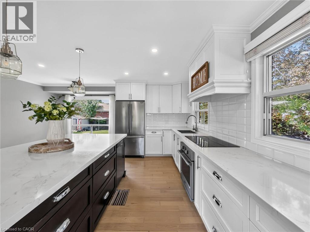 Kitchen featuring white upper cabinetry, a dark wood-finish island with a light countertop, stainless steel appliances, wood-finish flooring, and a subway tile backsplash - 143 Cromwell Crescent, Hamilton, ON - Indoor Photo Showing Kitchen With Upgraded Kitchen