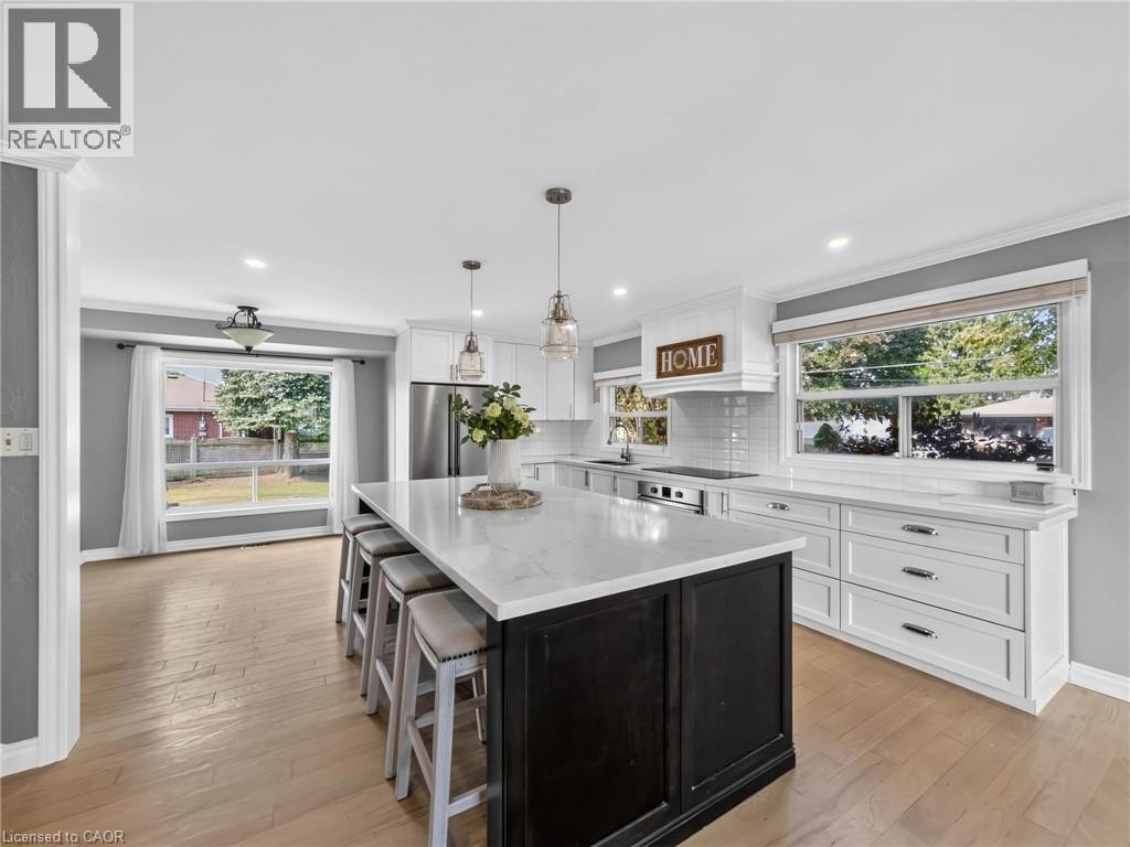 Kitchen featuring a large island with seating, white shaker cabinetry, stainless steel appliances, wood-finish flooring, and ample natural light from multiple windows - 143 Cromwell Crescent, Hamilton, ON - Indoor Photo Showing Kitchen With Upgraded Kitchen