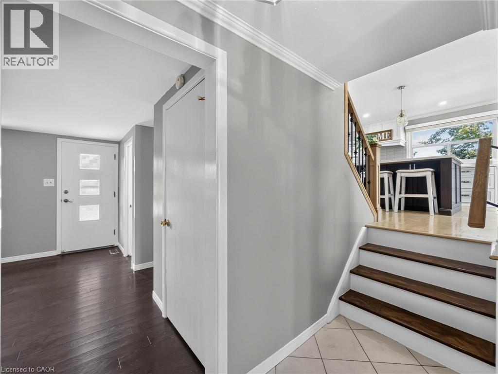 Entryway featuring dark wood-finish flooring, a modern white door with frosted glass panels, and a staircase with wood treads and a black metal spindle railing - 143 Cromwell Crescent, Hamilton, ON - Indoor Photo Showing Other Room