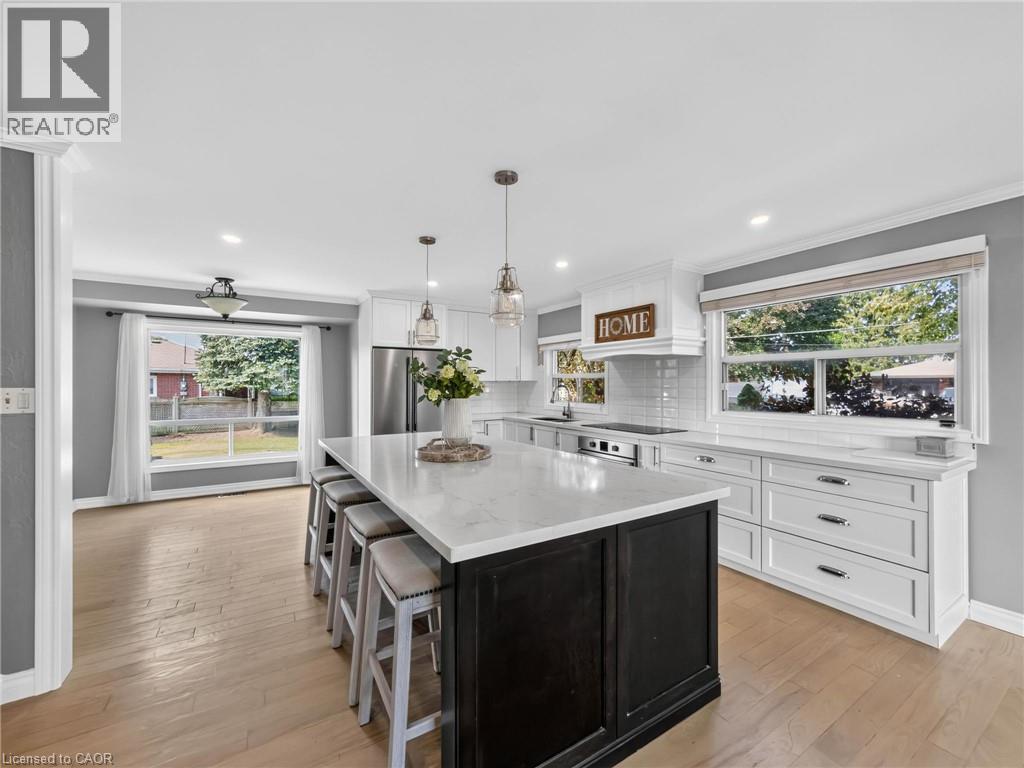 Kitchen featuring a large island with seating, white shaker cabinetry, stainless steel appliances, wood-finish flooring, and ample natural light from multiple windows - 143 Cromwell Crescent, Hamilton, ON - Indoor Photo Showing Kitchen With Upgraded Kitchen