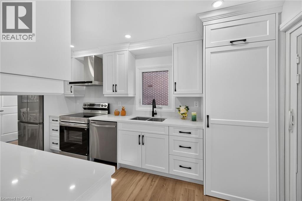 Contemporary kitchen featuring white cabinetry, stainless steel appliances, a paneled refrigerator, wood-finish flooring, and recessed lighting - 101 Loyalist Drive, Hamilton, ON - Indoor Photo Showing Kitchen With Double Sink