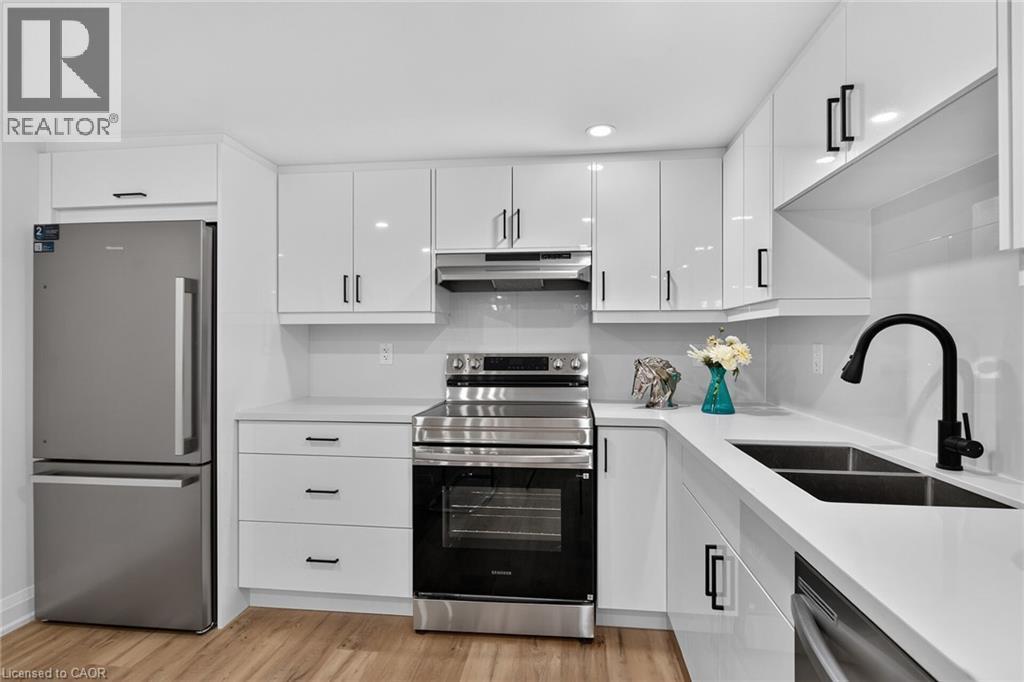 Contemporary kitchen featuring white flat-panel cabinetry with black hardware, white countertops, and wood-finish flooring - 101 Loyalist Drive, Hamilton, ON - Indoor Photo Showing Kitchen With Double Sink With Upgraded Kitchen