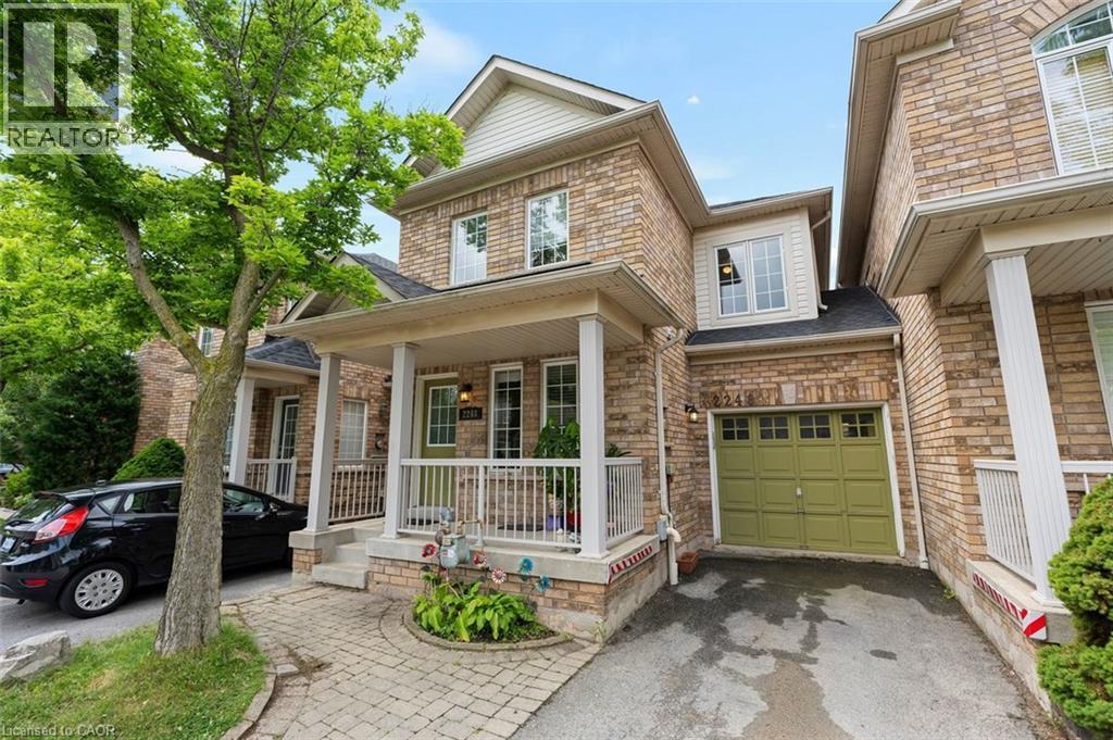 Brick facade residence featuring a covered front porch with white railings, a stone walkway, and an integrated single-car garage with a green door - 2248 Seton Crescent, Burlington, ON - Outdoor With Deck Patio Veranda