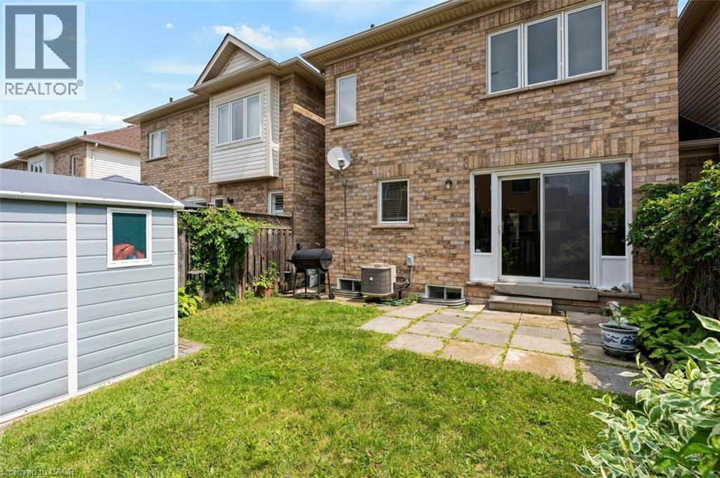 Expansive backyard featuring a manicured lawn, a detached storage shed, a stone paver patio, and sliding glass door access to the interior - 2248 Seton Crescent, Burlington, ON - Outdoor With Exterior